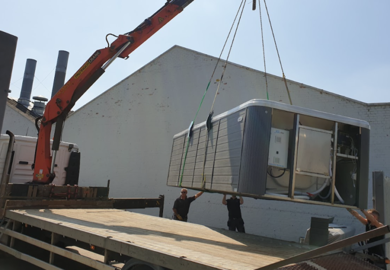 A professional crane lifting a large grey hot tub onto a flatbed truck for relocation at Birchanger Industrial Estate.