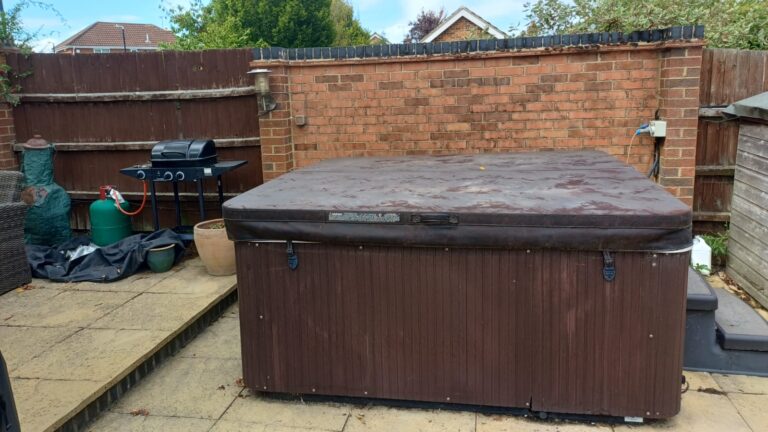 Older brown wood-effect hot tub with a weathered cover sitting on a patio, awaiting professional removal and disposal by Spa Wars.